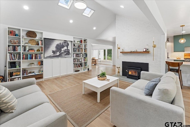 living room with high vaulted ceiling, light hardwood / wood-style floors, a skylight, and a fireplace