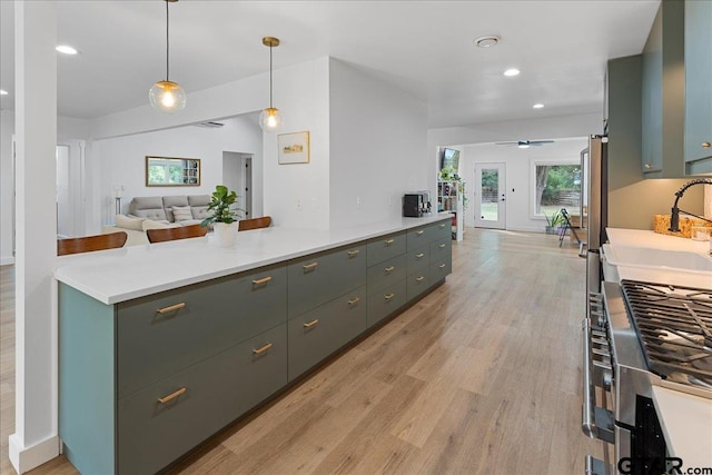 kitchen with stainless steel gas range oven, ceiling fan, light wood-type flooring, pendant lighting, and sink