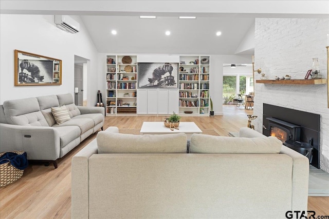 living room featuring vaulted ceiling, a wall mounted AC, a fireplace, and light hardwood / wood-style flooring