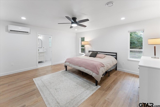 bedroom featuring ceiling fan, ensuite bathroom, light hardwood / wood-style floors, and a wall mounted air conditioner