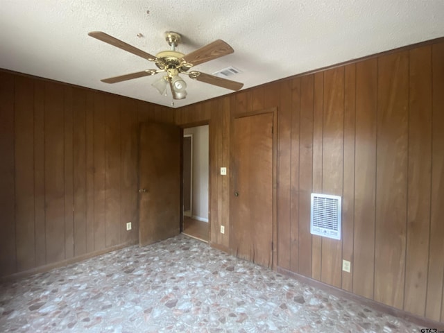 spare room featuring ceiling fan, wooden walls, and a textured ceiling