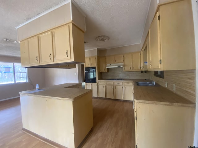 kitchen with light hardwood / wood-style floors, kitchen peninsula, a textured ceiling, light brown cabinetry, and oven