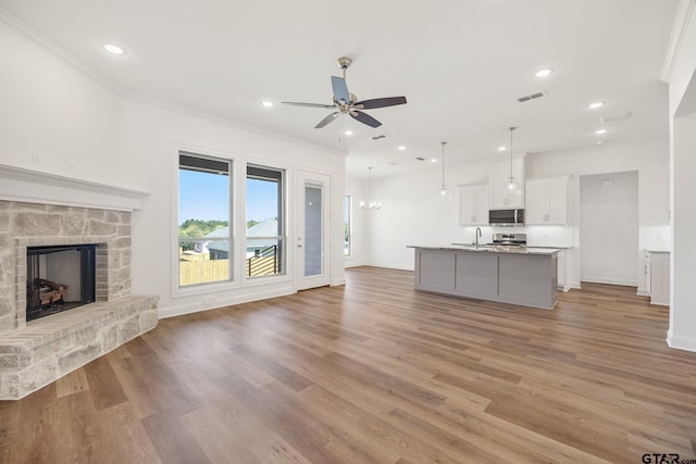 unfurnished living room with a fireplace, ceiling fan, light wood-type flooring, and crown molding