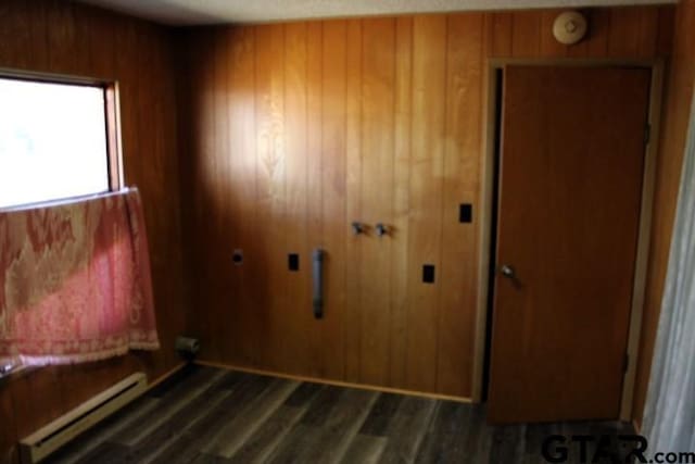 307 Lowry St, Arp, TX 75750 - unfurnished bedroom with baseboard heating, wooden walls, dark wood-type flooring, and a closet