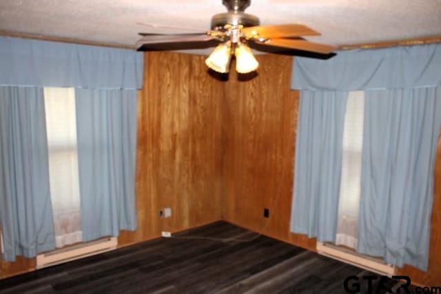 unfurnished room featuring a textured ceiling, wooden walls, ceiling fan, and dark wood-type flooring