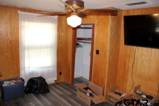 bedroom featuring ceiling fan, dark hardwood / wood-style floors, and wooden walls