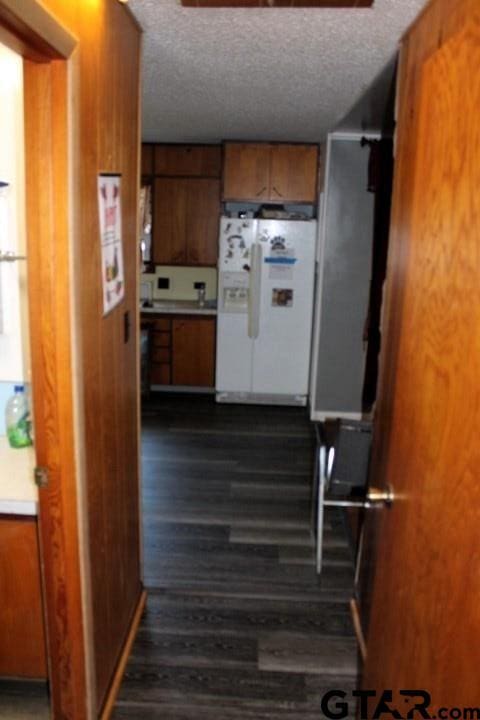 307 Lowry St, Arp, TX 75750 - kitchen with freestanding refrigerator, brown cabinetry, dark wood-style flooring, and a textured ceiling