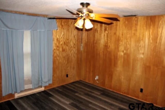 unfurnished room featuring a textured ceiling, dark wood-type flooring, ceiling fan, and wooden walls