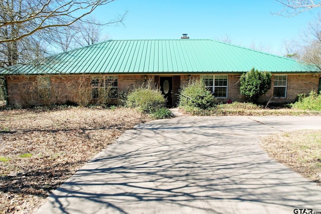 view of front of home featuring a chimney, metal roof, and brick siding