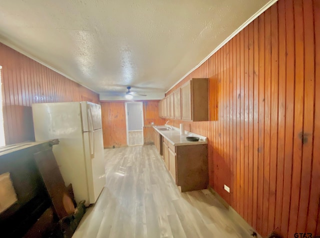 kitchen featuring sink, white refrigerator, crown molding, a textured ceiling, and light hardwood / wood-style flooring