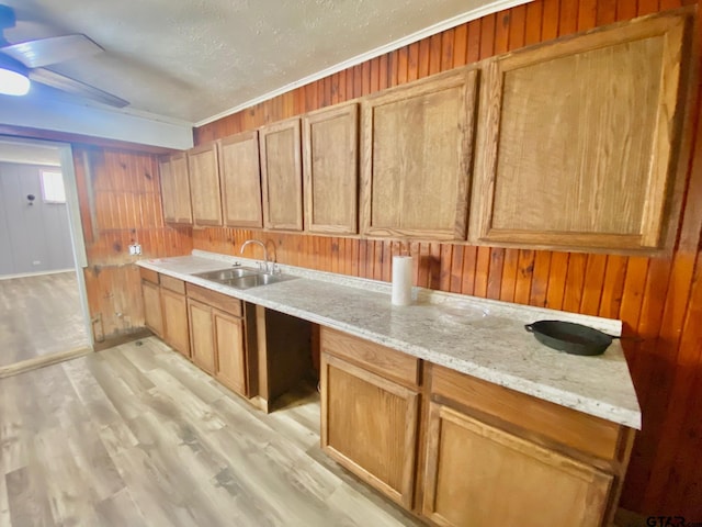 kitchen with sink, light stone counters, a textured ceiling, light wood-type flooring, and wooden walls