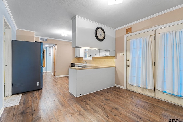 kitchen with ornamental molding, wood finished floors, freestanding refrigerator, light countertops, and white cabinetry