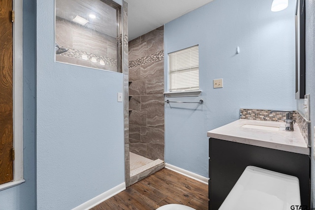 full bathroom with toilet, wood finished floors, vanity, baseboards, and tiled shower