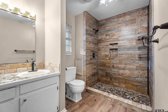 full bath with a tile shower, vanity, toilet, and wood finished floors