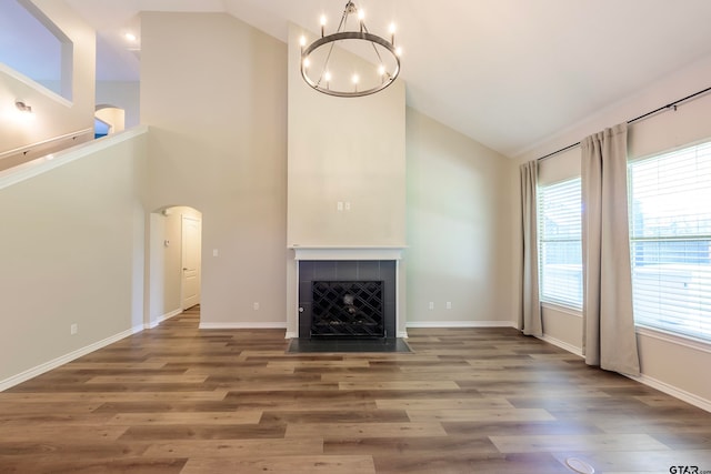 unfurnished living room featuring hardwood / wood-style flooring, a notable chandelier, a healthy amount of sunlight, and a tiled fireplace