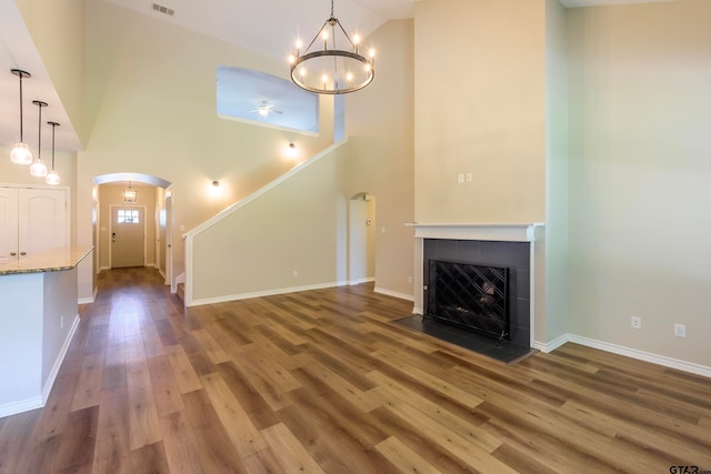 unfurnished living room with a tiled fireplace, high vaulted ceiling, a chandelier, and hardwood / wood-style flooring