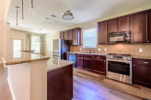 kitchen featuring light stone counters, appliances with stainless steel finishes, decorative light fixtures, a kitchen island, and light wood-type flooring