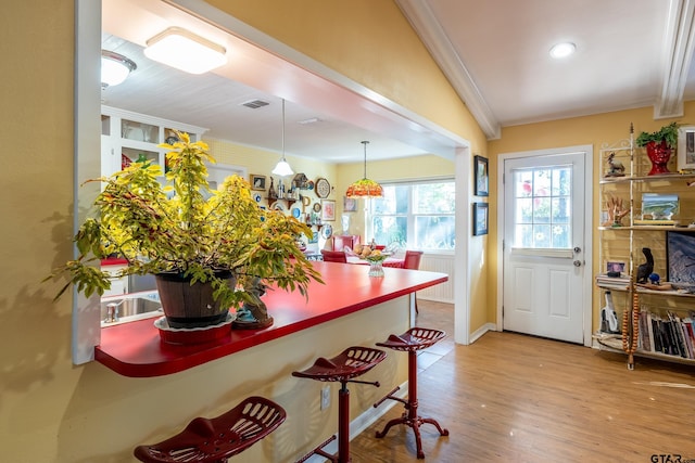 kitchen with vaulted ceiling, decorative light fixtures, crown molding, and light hardwood / wood-style floors