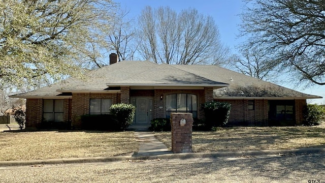 view of front of home with brick siding, a chimney, and roof with shingles