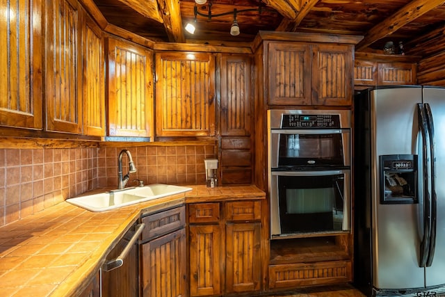 kitchen with appliances with stainless steel finishes, sink, tile counters, and decorative backsplash