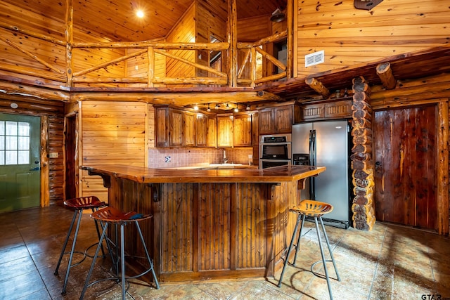 kitchen featuring a towering ceiling, log walls, backsplash, kitchen peninsula, and stainless steel appliances