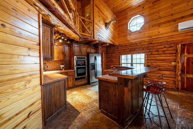 kitchen featuring a breakfast bar, a towering ceiling, a wall unit AC, stainless steel appliances, and kitchen peninsula