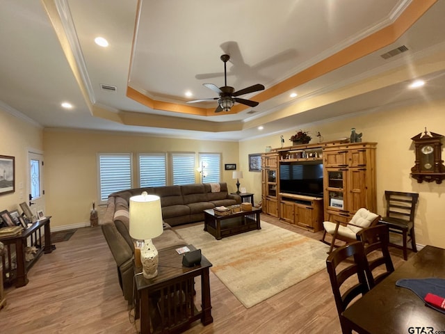 living room featuring light wood-type flooring, ornamental molding, and a raised ceiling