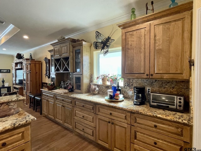 kitchen with tasteful backsplash, hardwood / wood-style flooring, crown molding, and light stone countertops