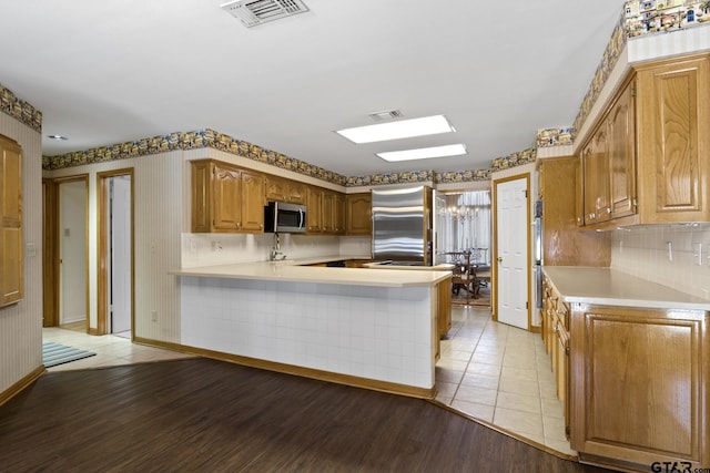 205 Turnberry Cir, Mount Pleasant, TX 75455 - kitchen with appliances with stainless steel finishes, a peninsula, light countertops, light wood-style floors, and brown cabinetry