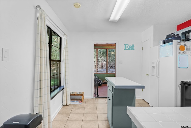 kitchen with a kitchen island, tile countertops, white refrigerator with ice dispenser, light tile patterned floors, and a textured ceiling