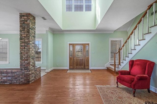 foyer entrance with wood-type flooring, a towering ceiling, and crown molding