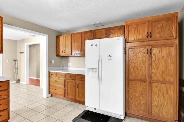 kitchen featuring white fridge with ice dispenser, light tile patterned floors, and a textured ceiling