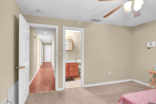 bedroom with ceiling fan, connected bathroom, light carpet, and a textured ceiling