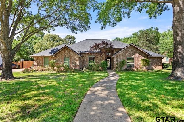 view of front of house featuring brick siding, fence, a front yard, and roof with shingles