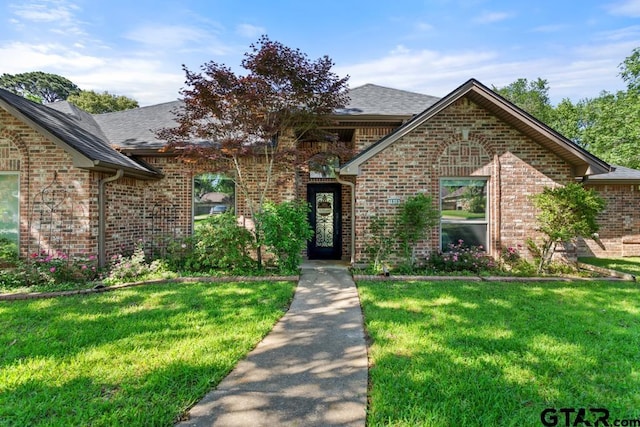 traditional-style house featuring brick siding, a front lawn, and roof with shingles