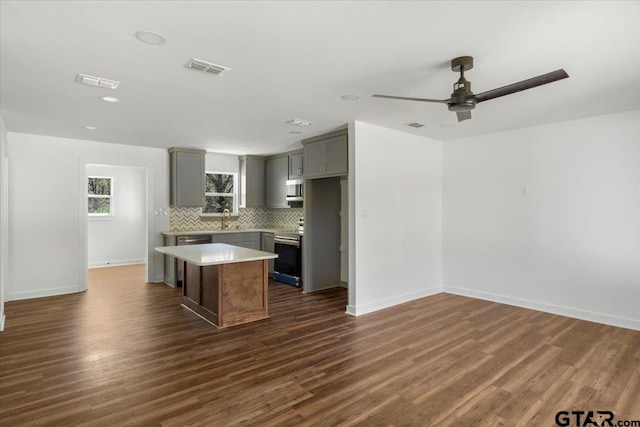 kitchen featuring a center island, dark wood-type flooring, decorative backsplash, gray cabinets, and stainless steel appliances