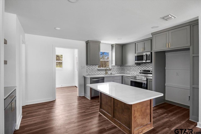 kitchen with dark wood-style floors, visible vents, gray cabinets, stainless steel appliances, and decorative backsplash