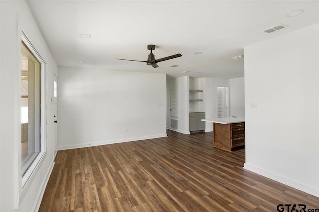 unfurnished living room featuring dark wood-type flooring, baseboards, visible vents, and ceiling fan