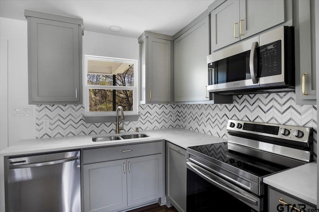 kitchen featuring backsplash, gray cabinets, stainless steel appliances, and a sink