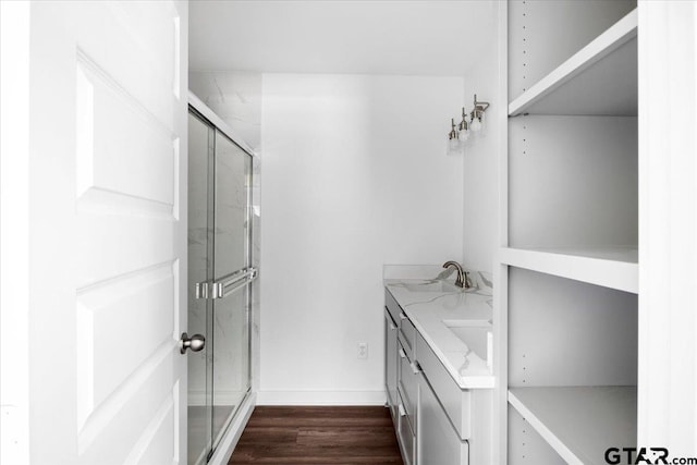 full bathroom featuring wood finished floors, baseboards, double vanity, a sink, and a shower stall