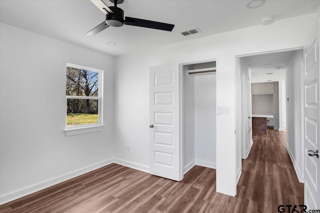 unfurnished bedroom with baseboards, visible vents, dark wood-style flooring, ceiling fan, and a closet