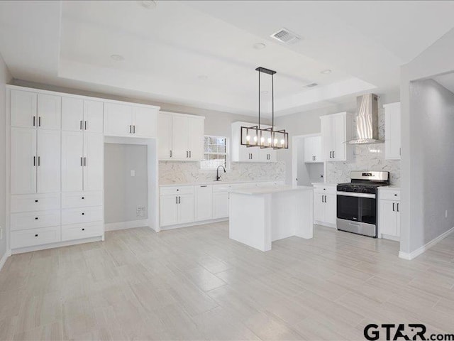 kitchen featuring stainless steel range with gas cooktop, a raised ceiling, light countertops, a sink, and wall chimney exhaust hood