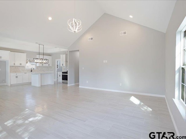 unfurnished living room with a notable chandelier, visible vents, a sink, high vaulted ceiling, and baseboards