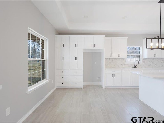 kitchen featuring baseboards, white cabinets, decorative light fixtures, light countertops, and a sink