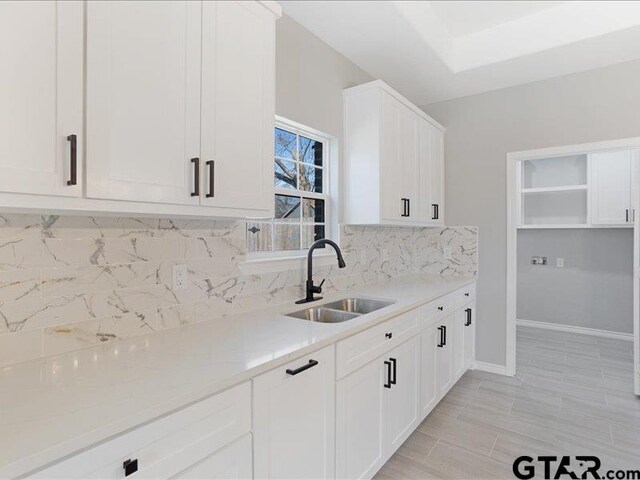 kitchen featuring tasteful backsplash, a sink, white cabinetry, and baseboards