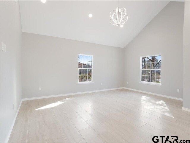 unfurnished room with baseboards, high vaulted ceiling, and a notable chandelier