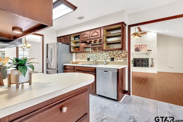 kitchen with decorative backsplash, appliances with stainless steel finishes, a brick fireplace, sink, and light hardwood / wood-style floors