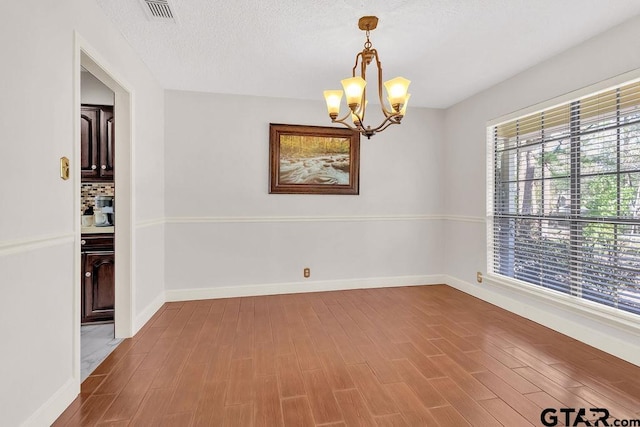 spare room featuring a textured ceiling, hardwood / wood-style flooring, and a notable chandelier