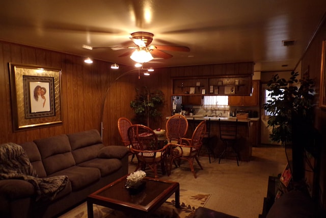 carpeted living room featuring ceiling fan and wooden walls