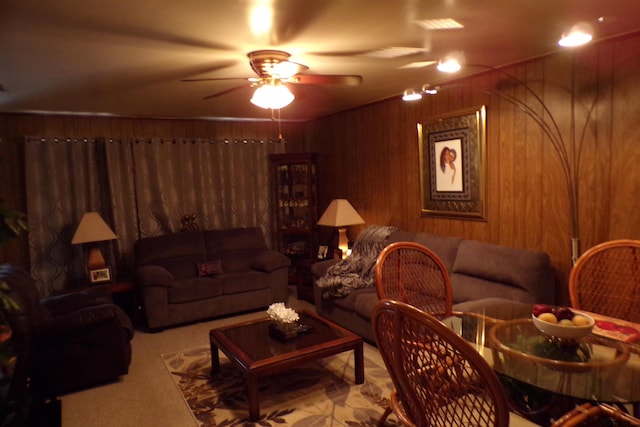 carpeted living room featuring wooden walls and ceiling fan